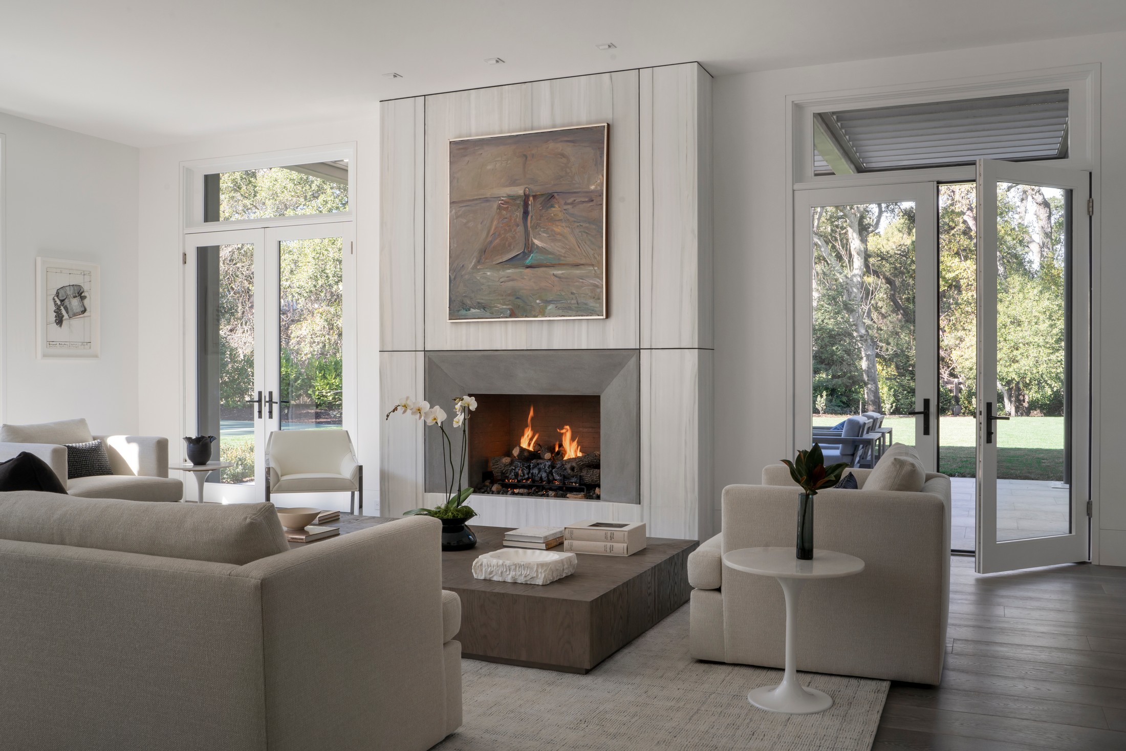 Living room area with a lit fireplace, stone low to the ground table with books and flowers on it. Multiple seats and couches.