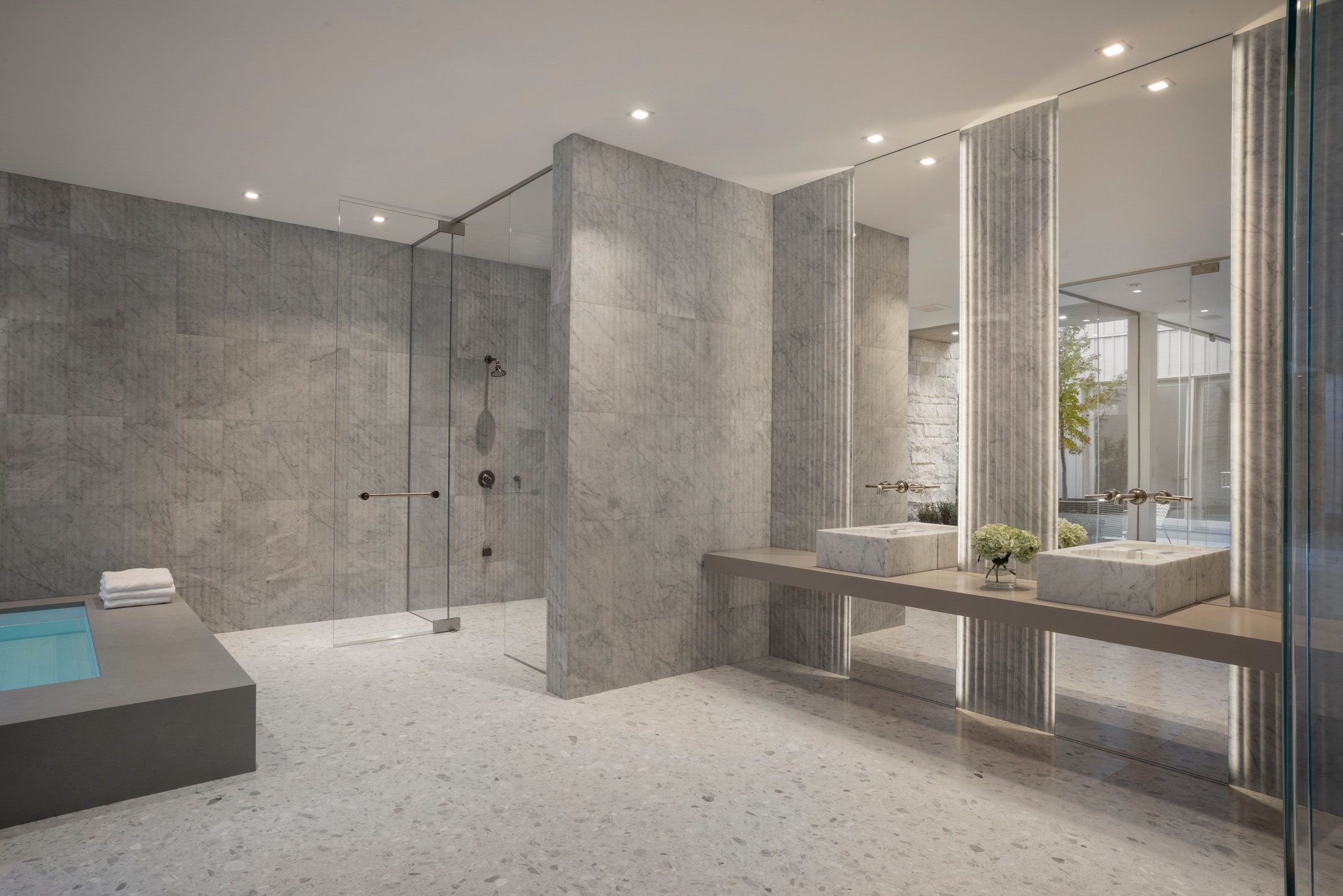 Large bathroom with shower, two marble sinks with vanity type lighting. There is a bathtub to the side.