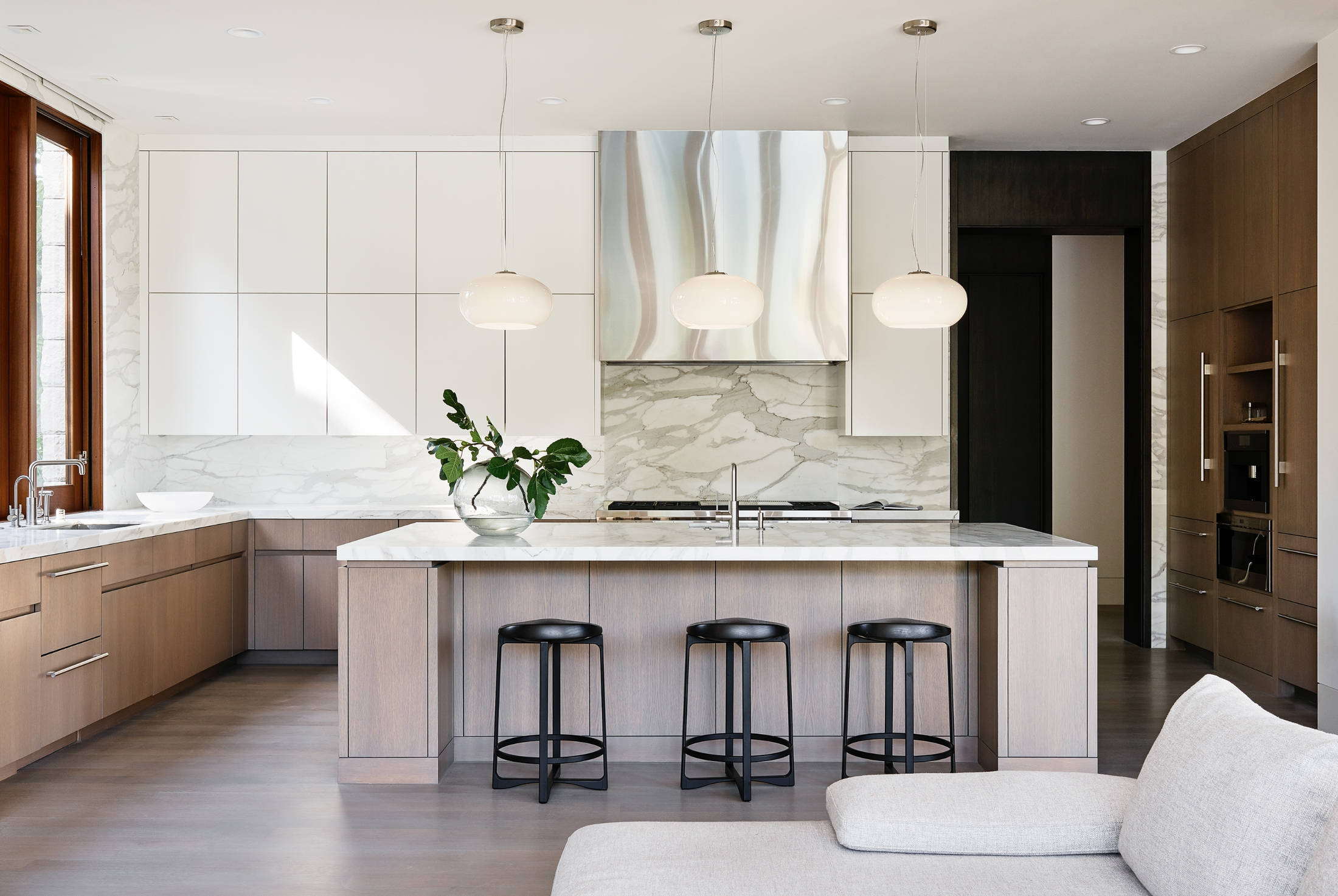 Kitchen with a large island, silver and white appliances, and black bar stools.