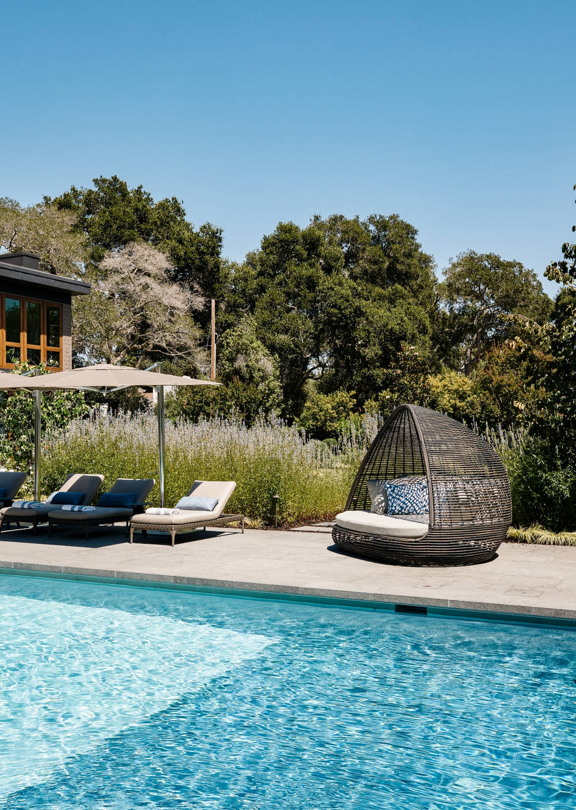 Pool area with large woven seats, lounge chairs, and umbrellas.