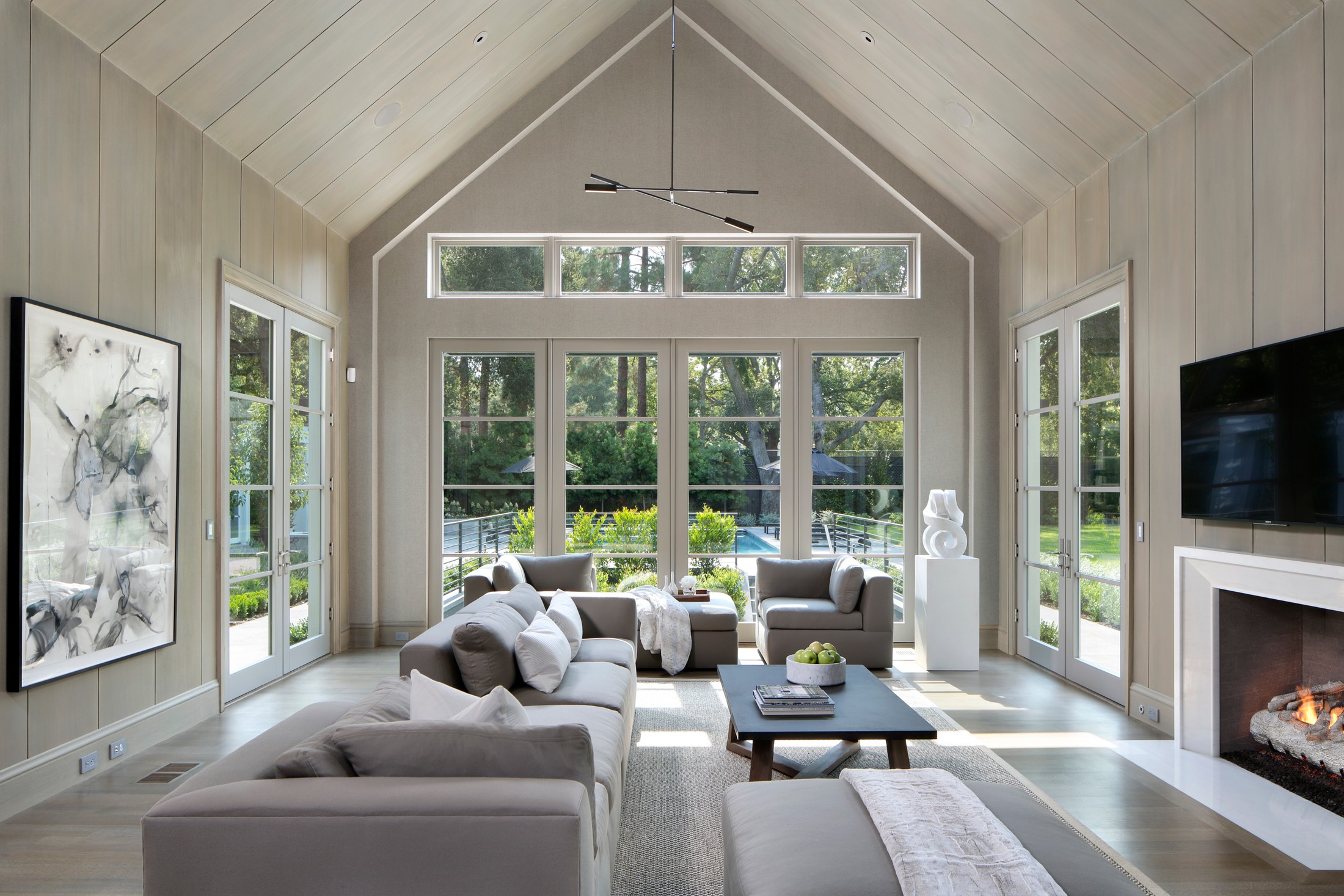 Living room space with vaulted ceilings, and seating area. There is a fireplace with a tv above it.