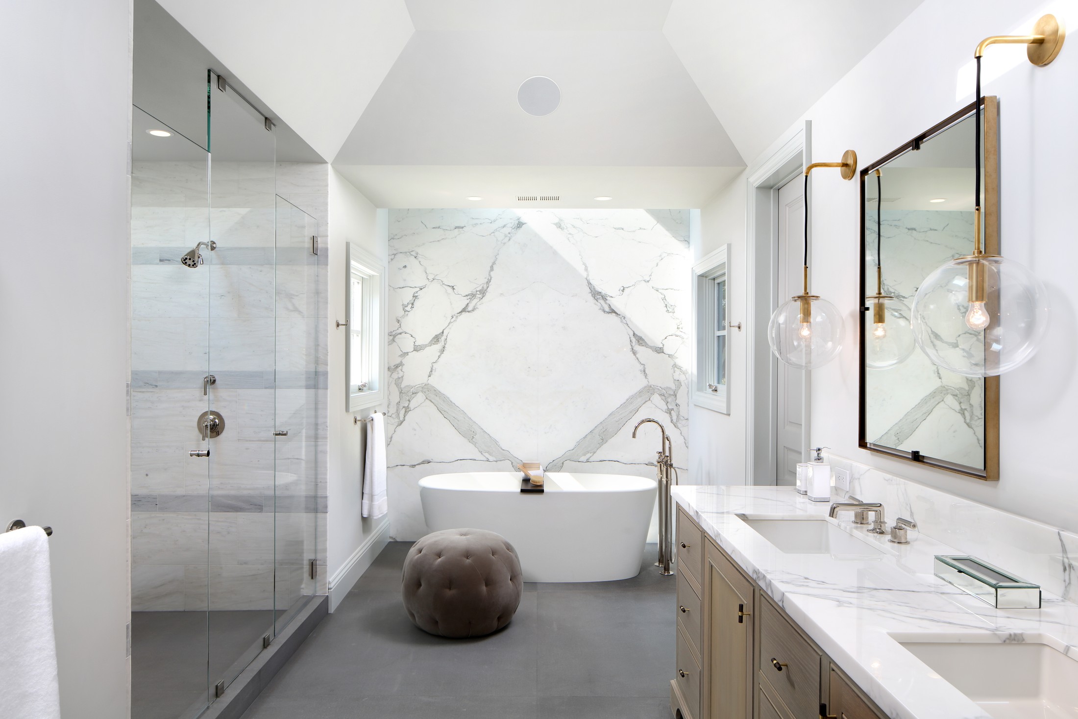 Bathroom with marble wall, glass shower, marble countertop for sinks, and a circular seat next to the white bathtub.