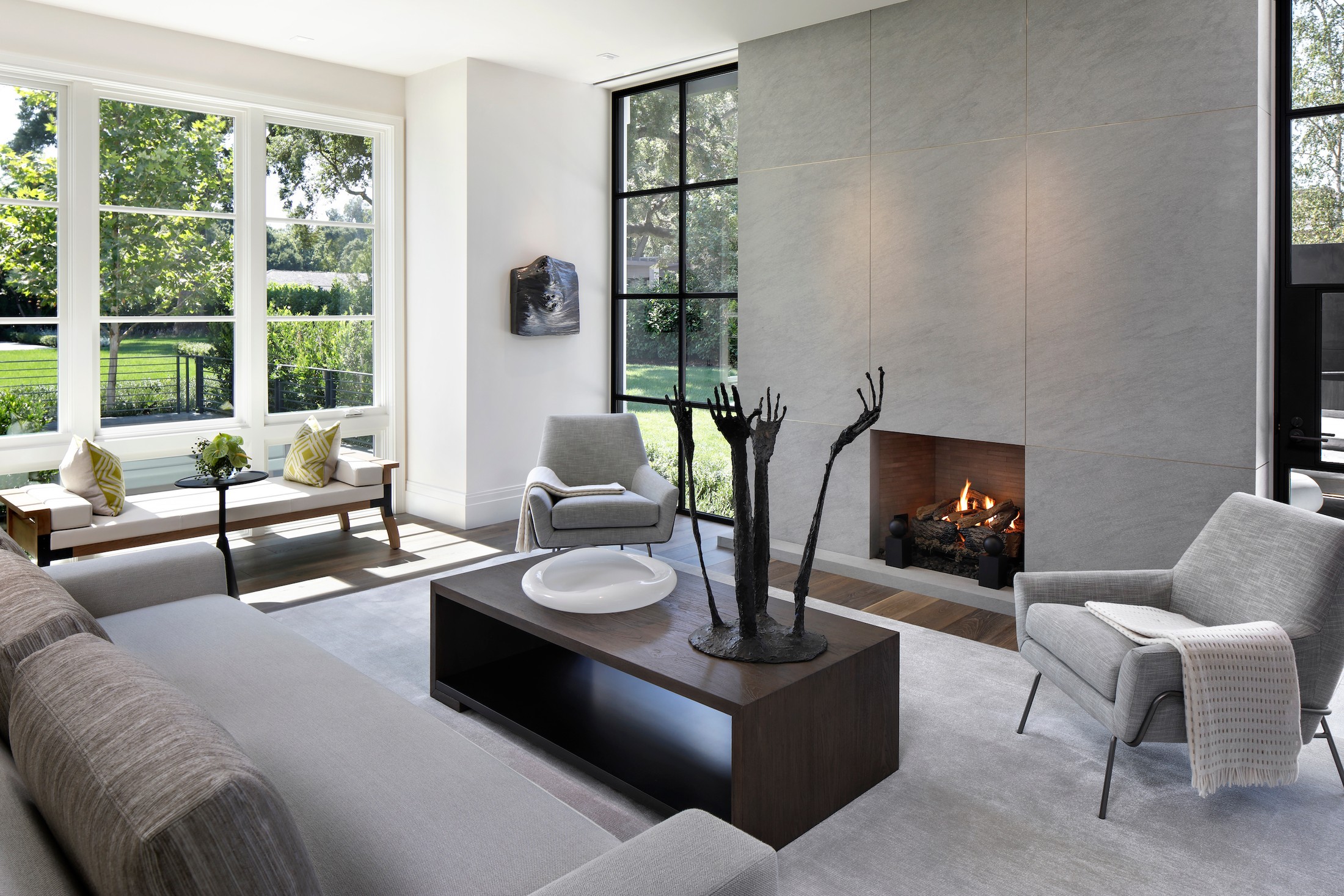 Living room space with lit fireplace, chairs and a sofa. The chairs have throw blankets laid on them. Hand sculpture and bowl are on the table in the center of the room.