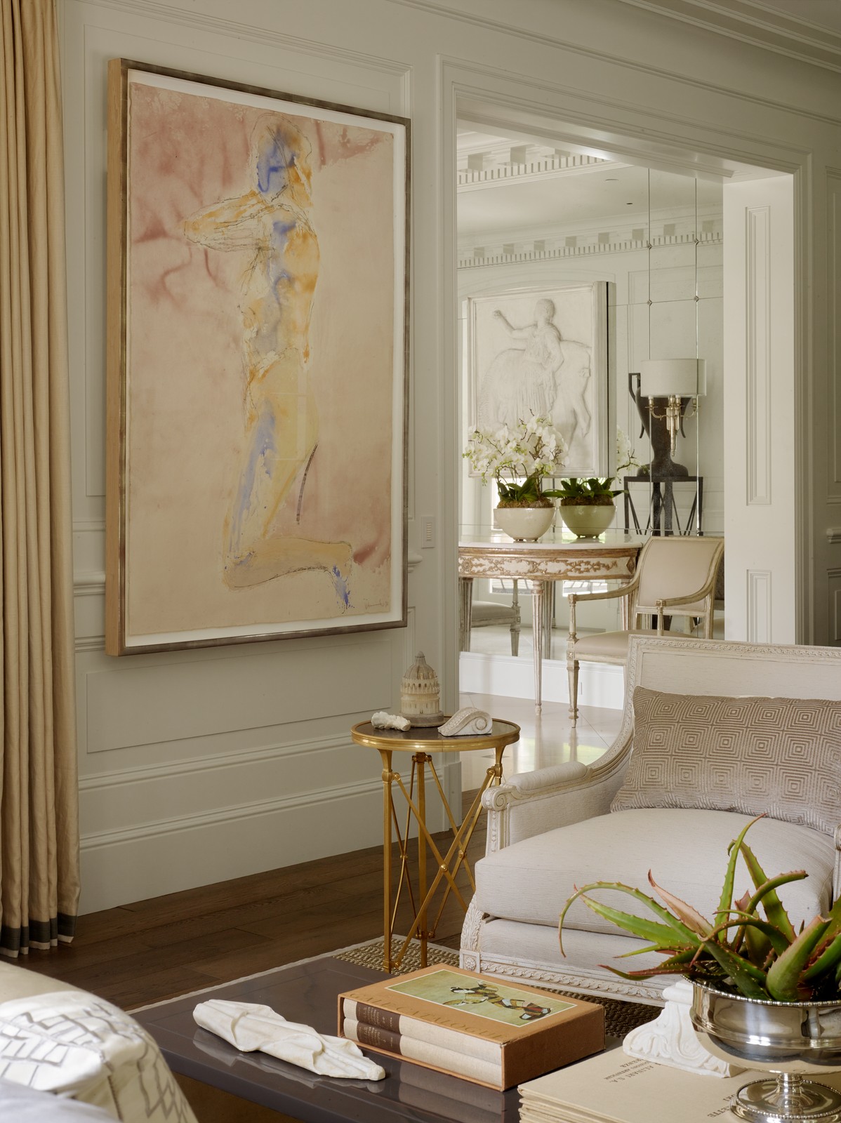 Living room area - there is a large painting of a silhouette of a body hanging on the wall. There are plants and flowers throughout the room, and books on the table.