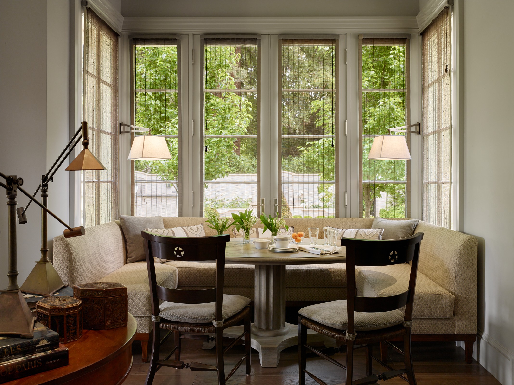 Kitchen nook with a U shaped sofa that fits perfectly into the nook. There is a table with plates and flowers and two additional chairs.