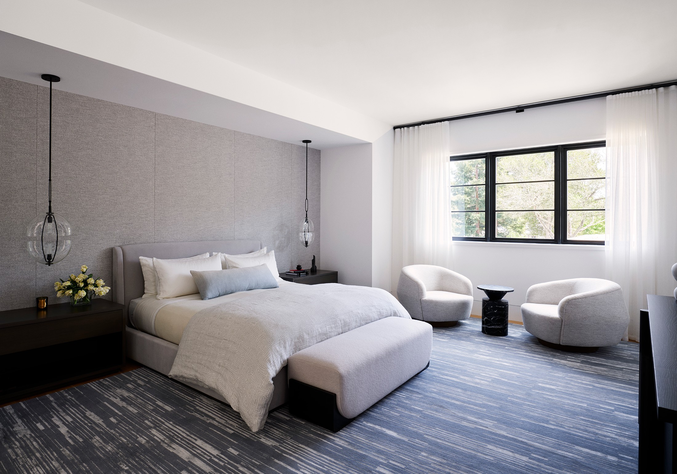 Bedroom with large black and clear lamps, flowers. There is a seating area with two circular chairs and a black desk next to the window.