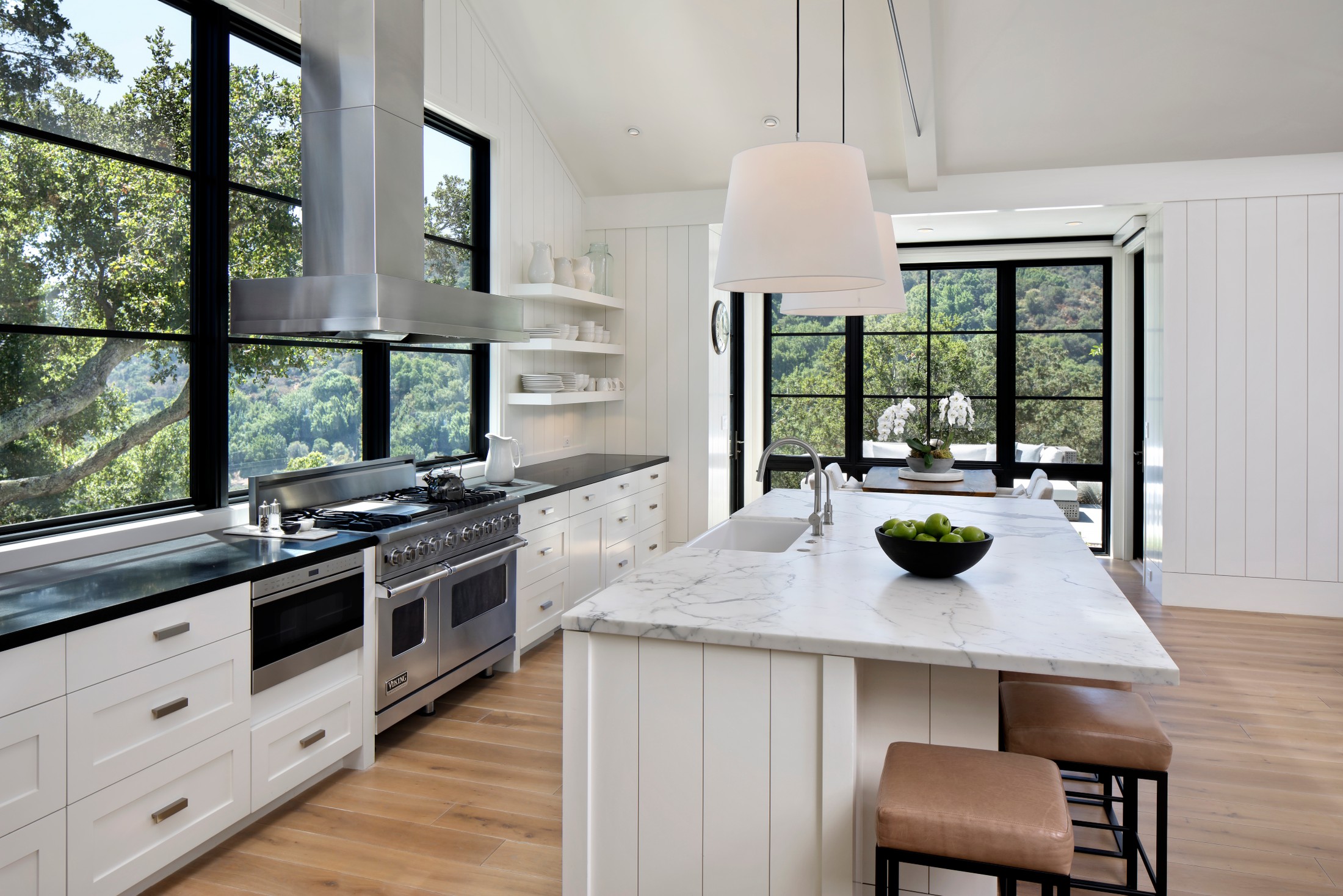 Kitchen with silver and white appliances, white marble and black marble countertops, and bar stools.
