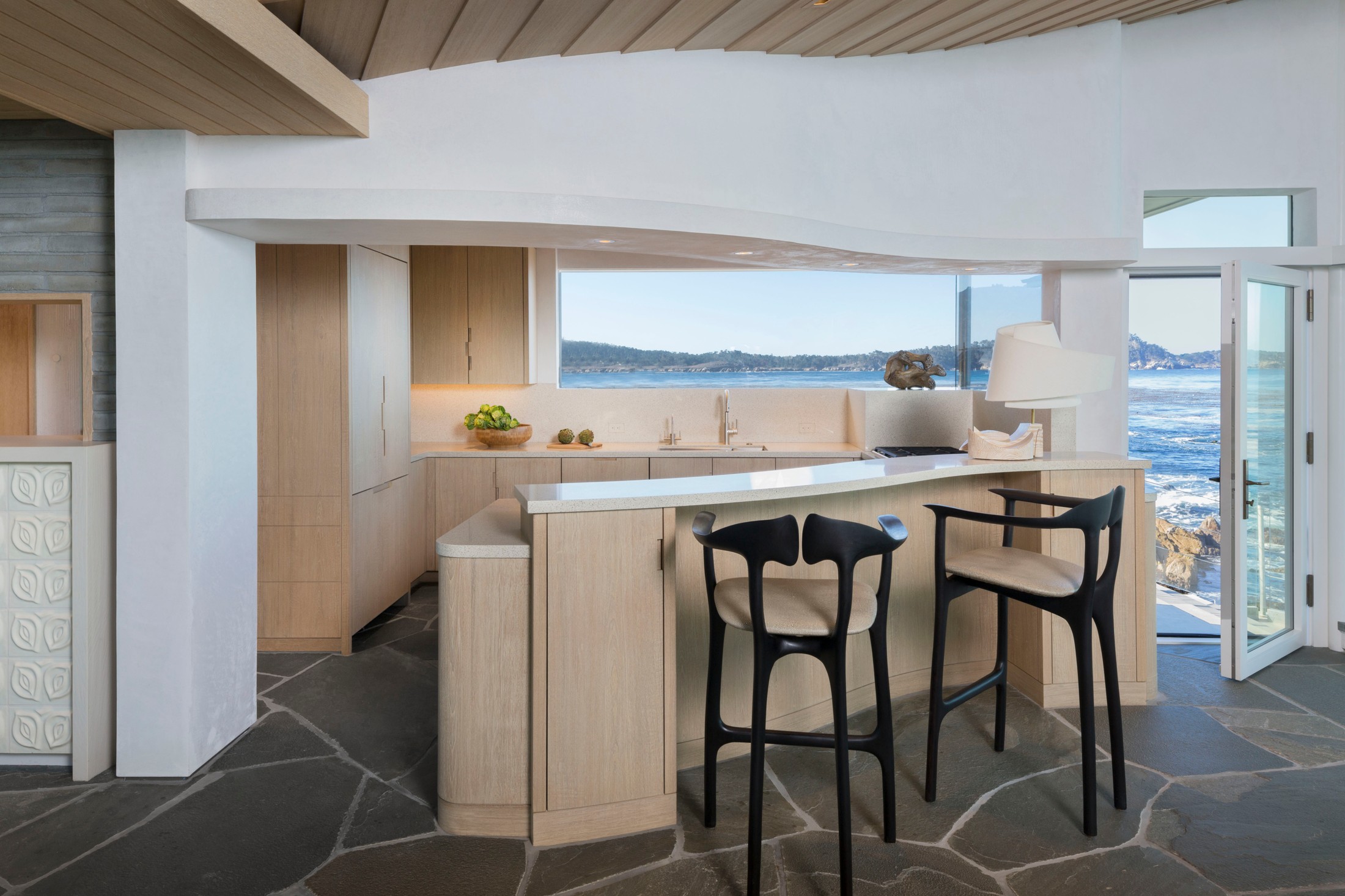 Small kitchen nook with light oak furniture, black and oak bar chairs, overlooking the ocean in the background.