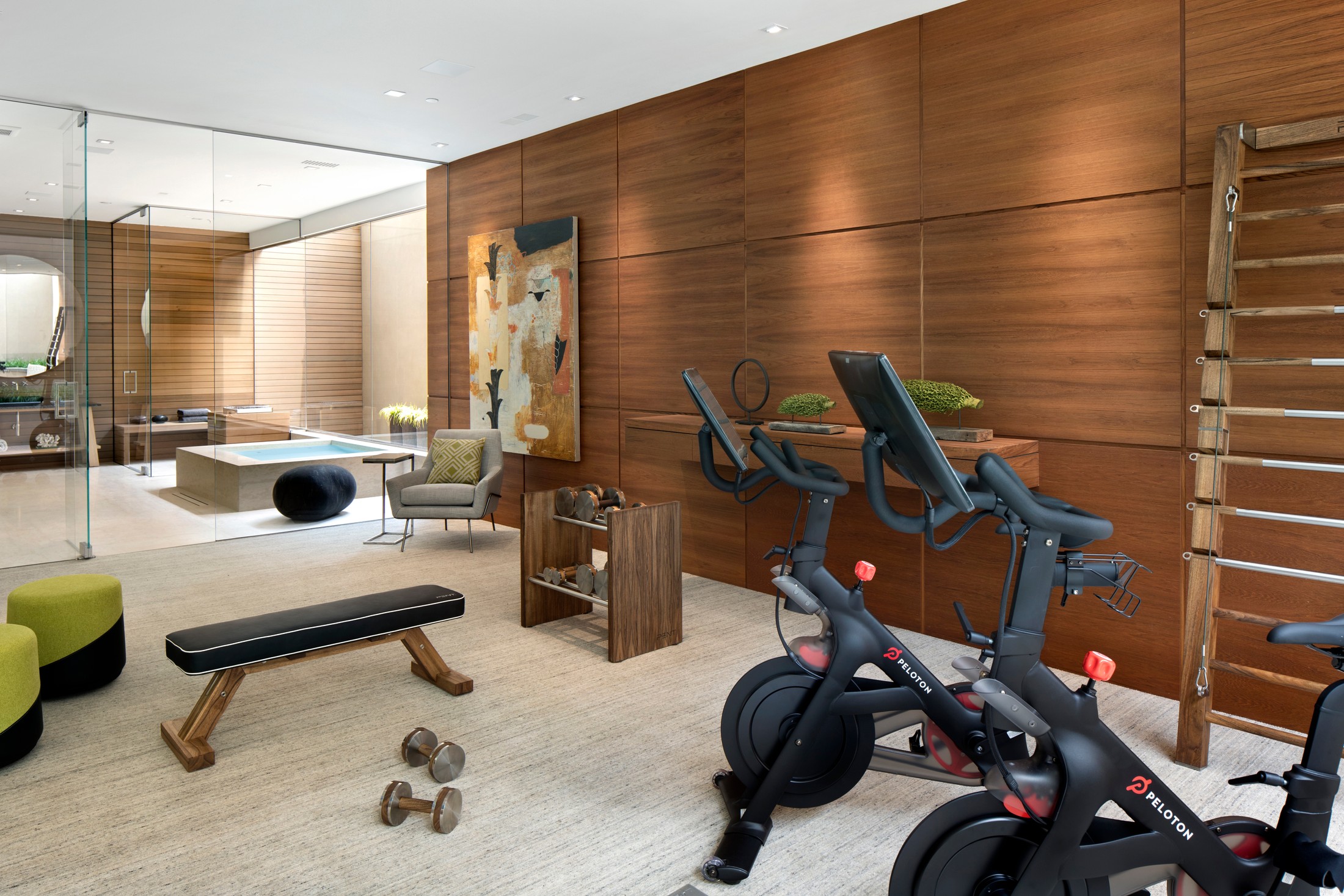 Exercise room with two peloton bikes, weights, artwork on the wooden wall. 
