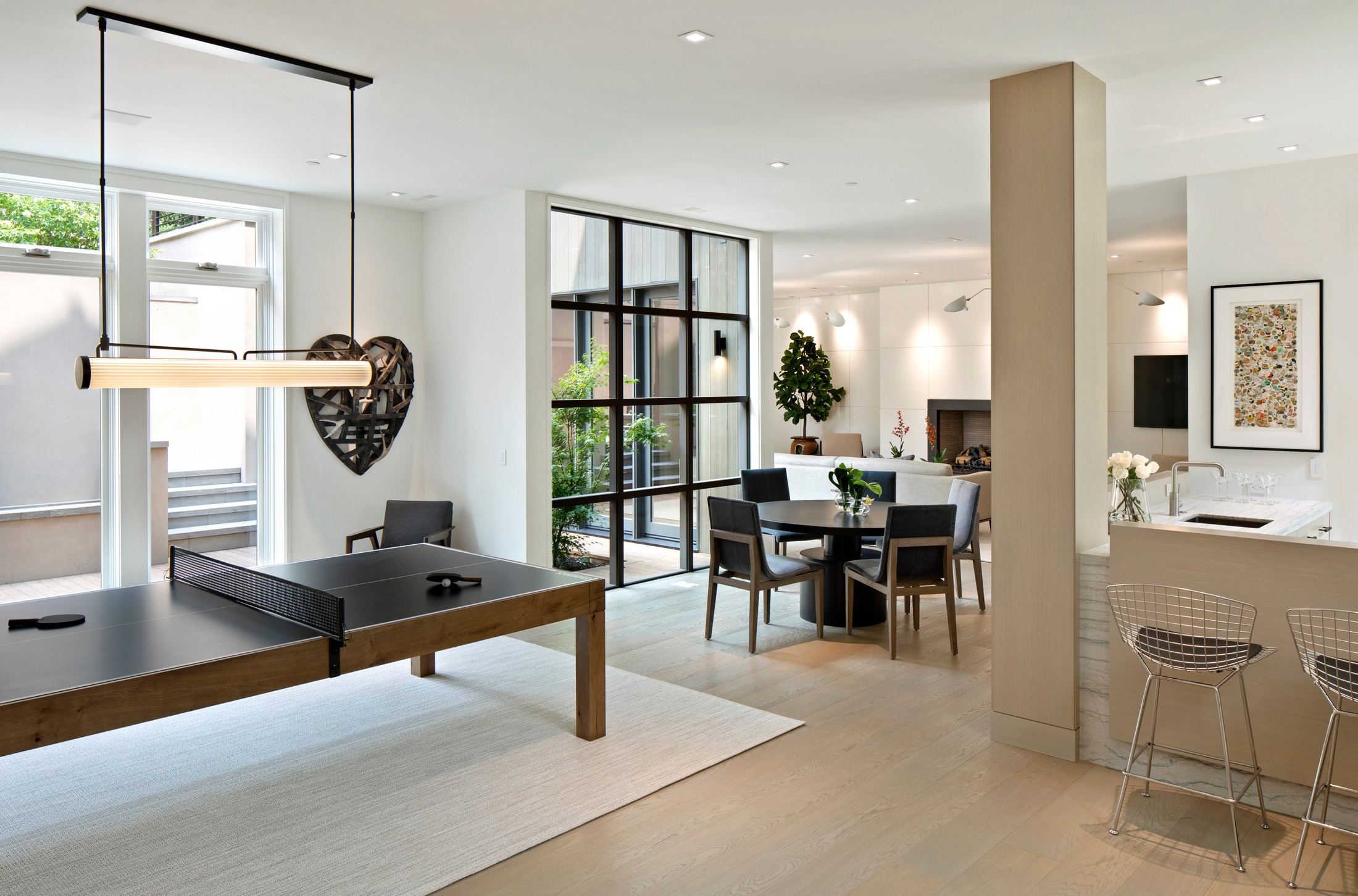 Lower level of the home, which includes a table with chairs, ping pong table, hanging lights, and windows with black detailing.