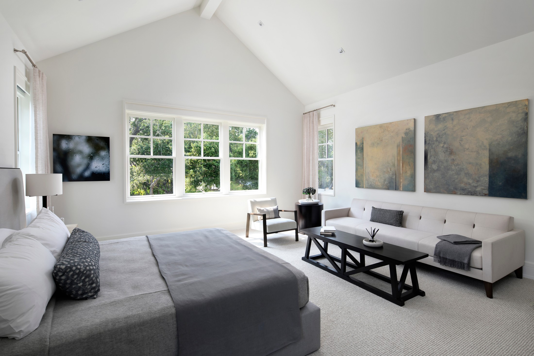 Master bedroom which includes vaulted ceilings, abstract artwork on the wall, a large sofa with a black table, textured rug, and a bed.