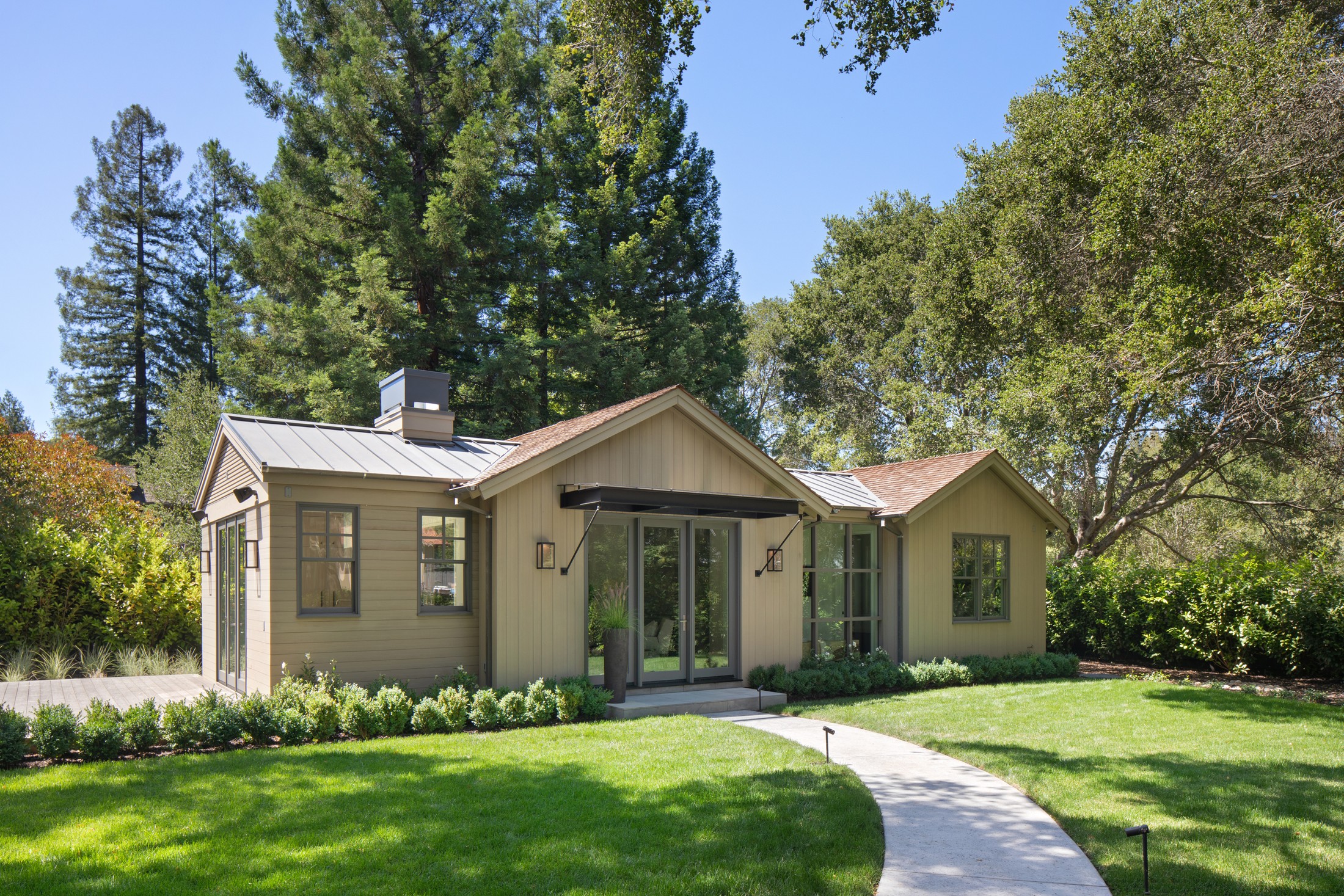 Exterior image of the guest house, focusing on the walkway into the front door. There is grass and trees surrounding the guest house.