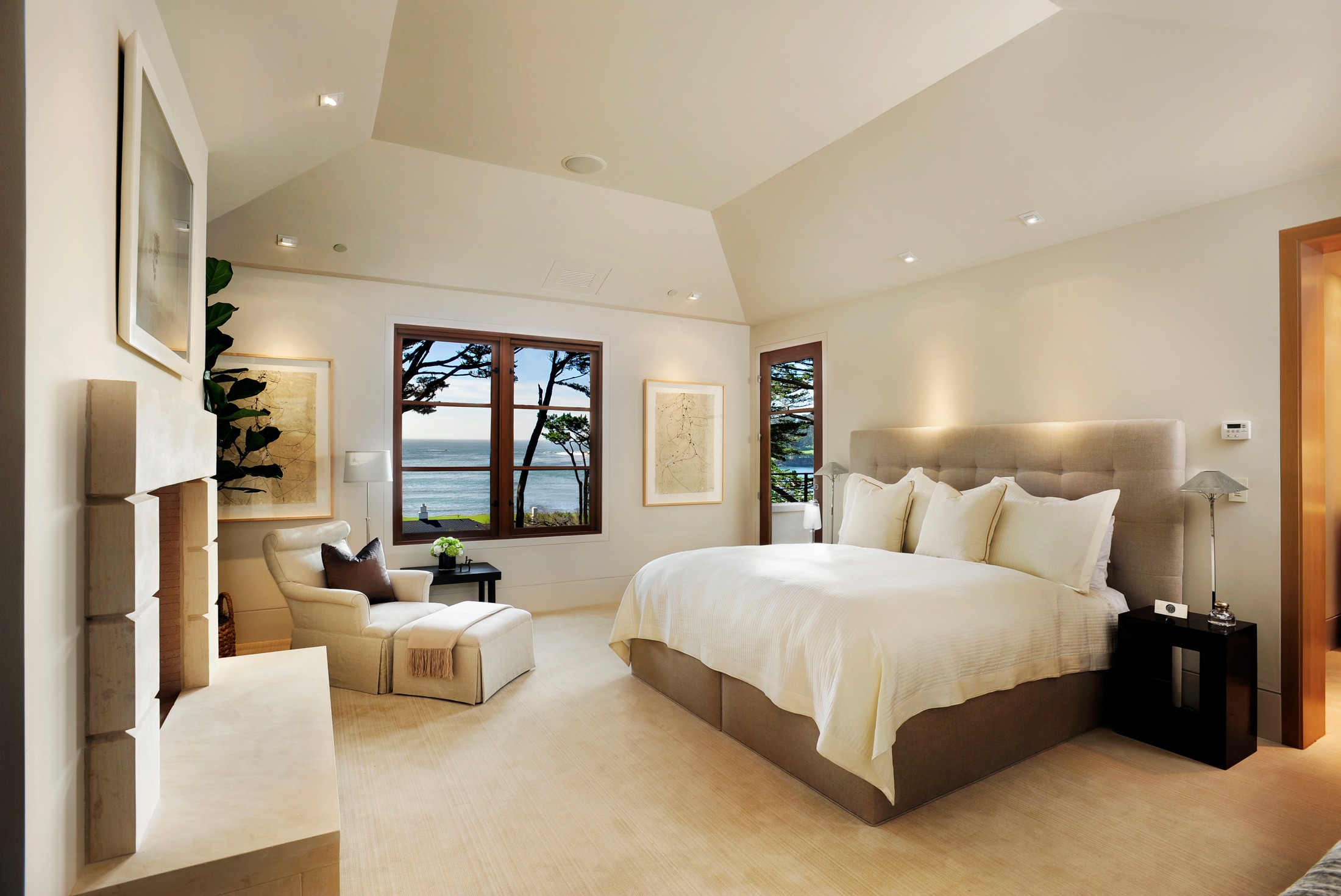 Bedroom which includes a fireplace, lounge chair, large bed, nightstand, windows and a door to a patio.