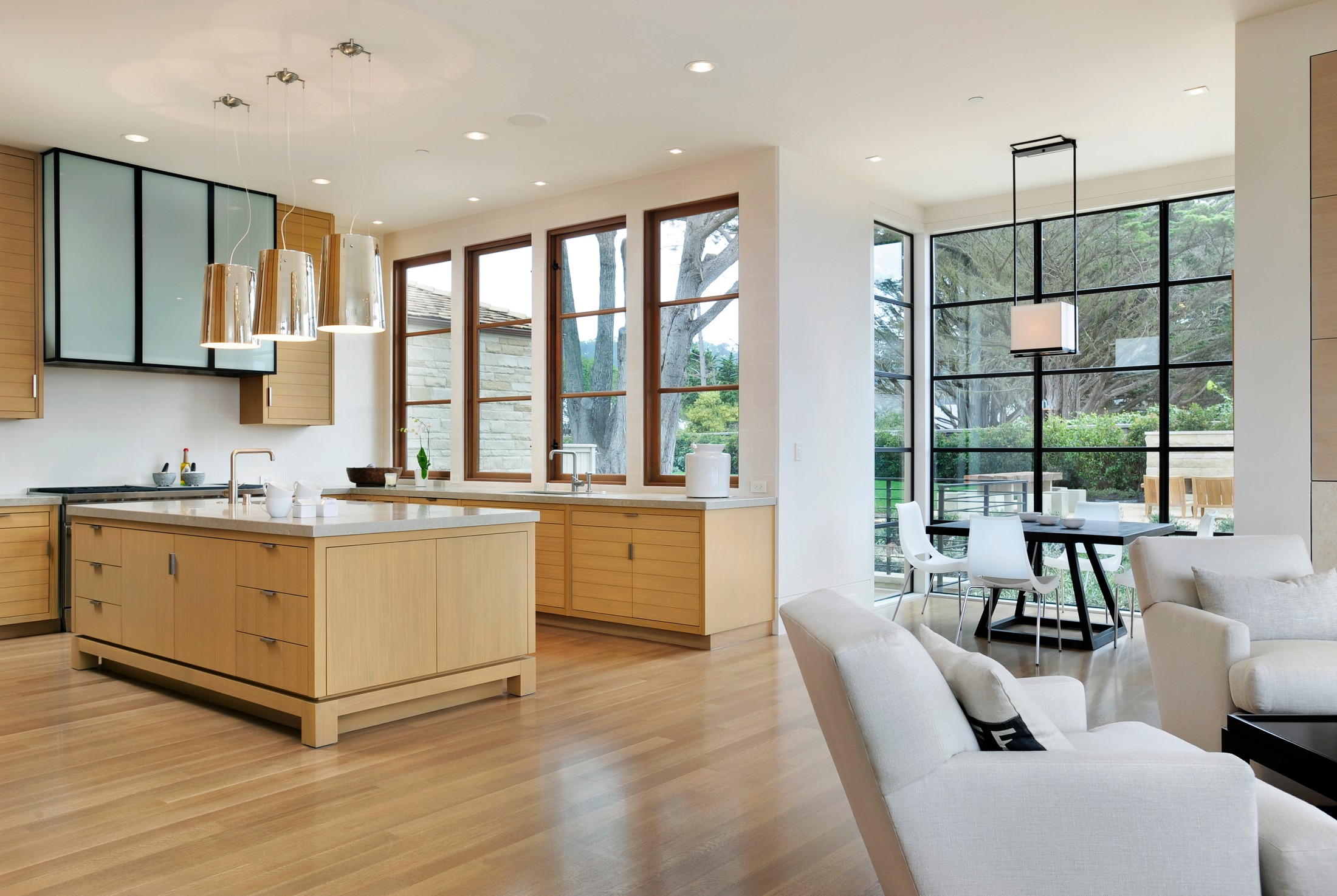Kitchen space with tall wooden windows, wood appliances and furniture, and off to the side of a living space with off-white furniture. There is a smaller section with seating to eat.