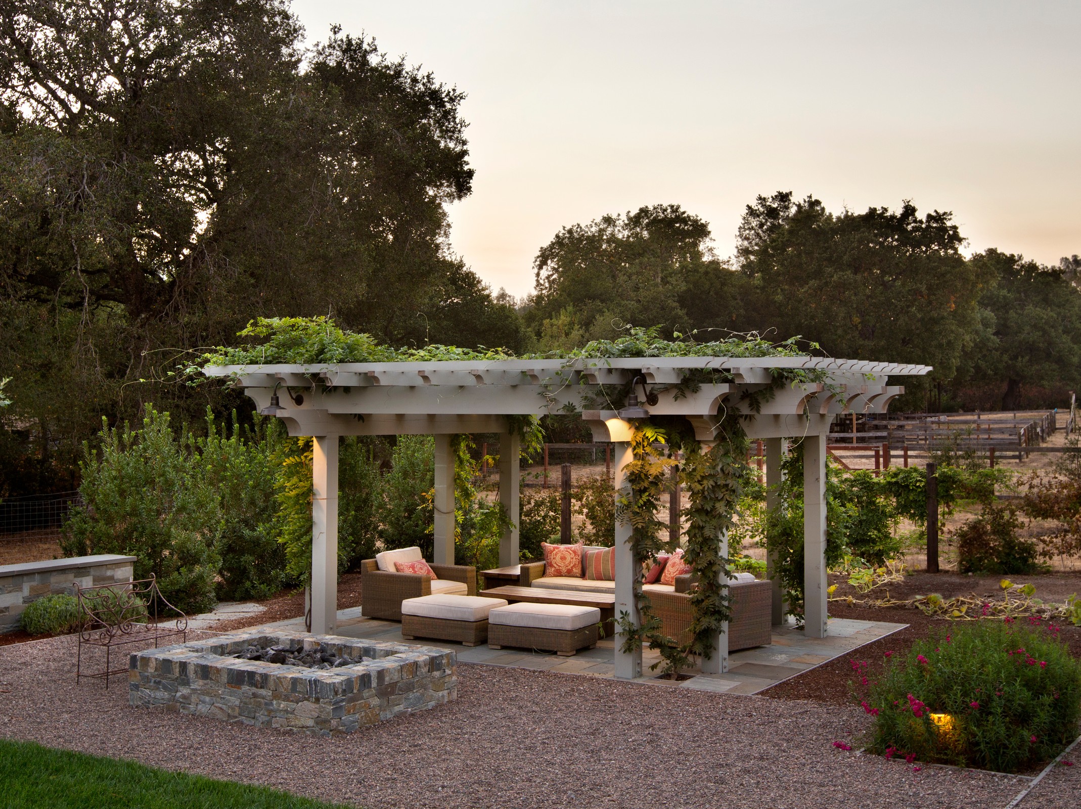 Image of an outdoor gazebo, with patio furniture. There is gravel and a firepit off to the side, and ivy hanging off of the gazebo.