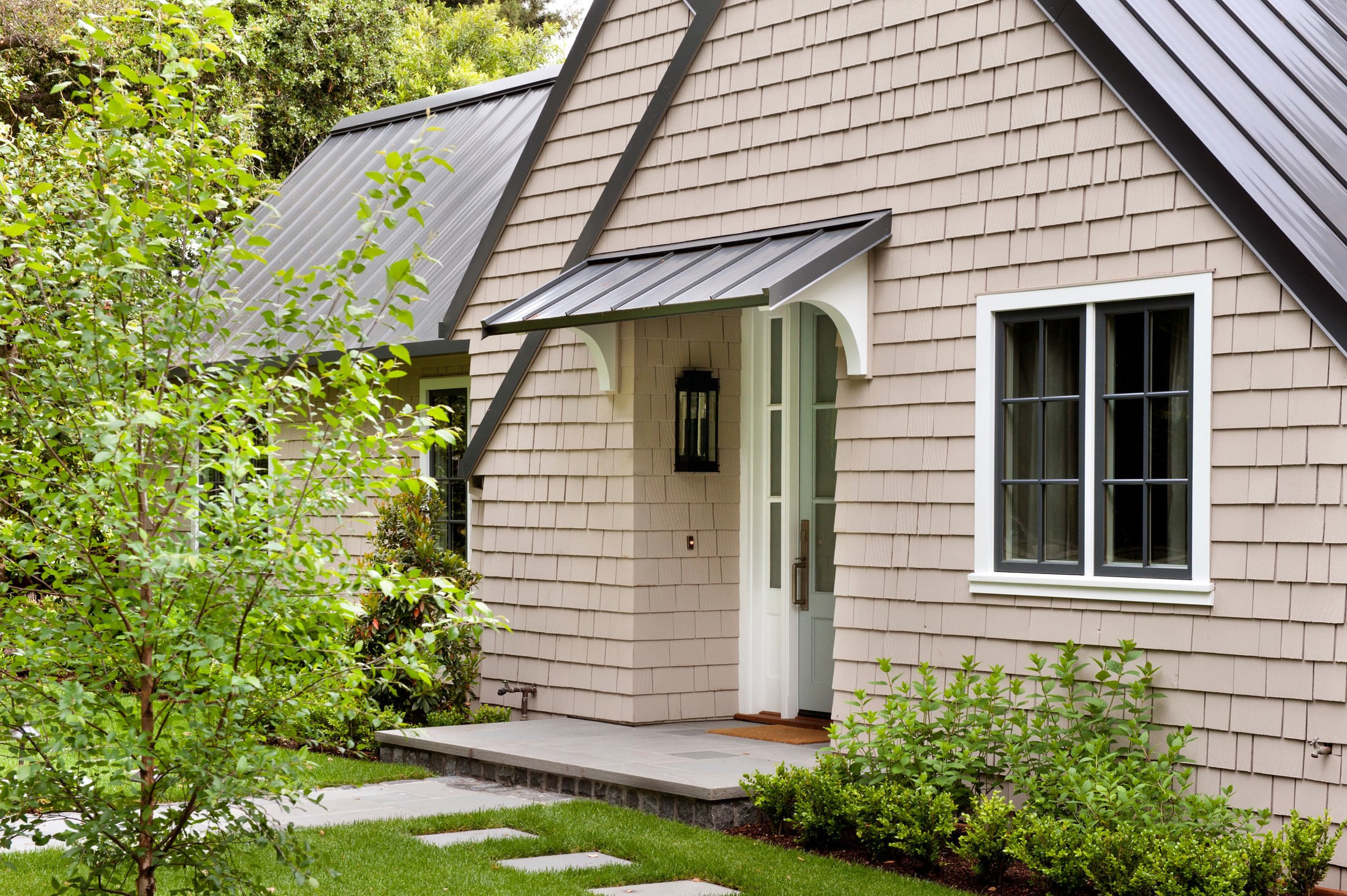 Closeup shot of the entranceway of the home There is a pair of windows to the side, and a small roof above the doorway.