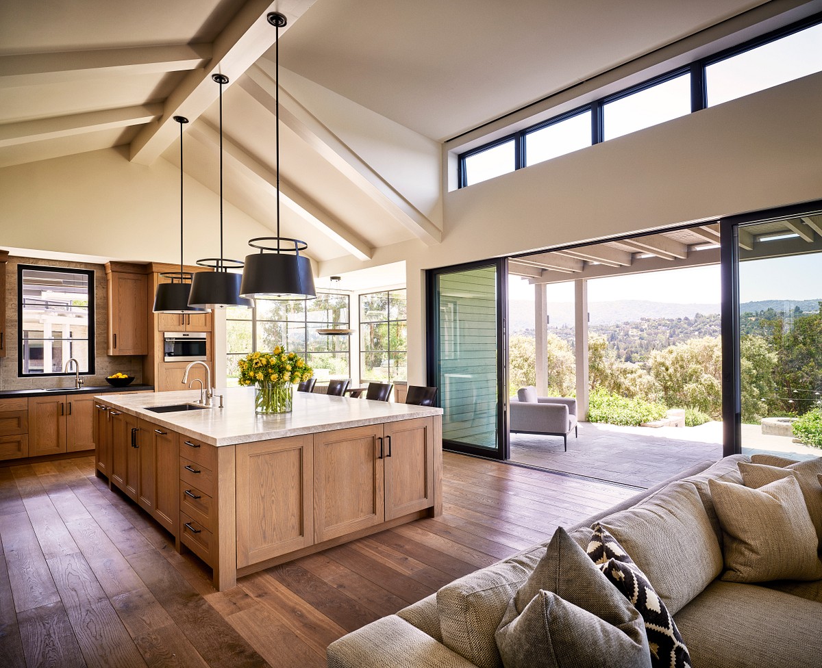 Image of a kitchen, which includes yellow flowers on the countertop. Large black lamps coming from the ceiling, and a big door which leads you to the backyard.