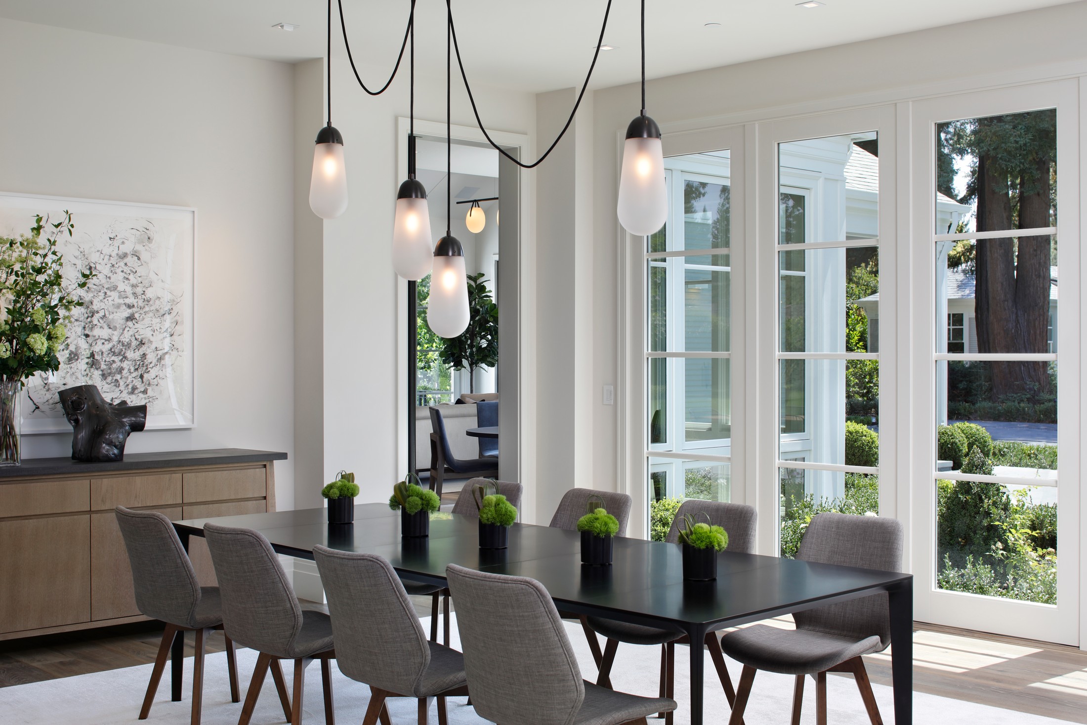 Close up of the living room with white/black dangling lamps from the ceiling, black table and grey chairs.