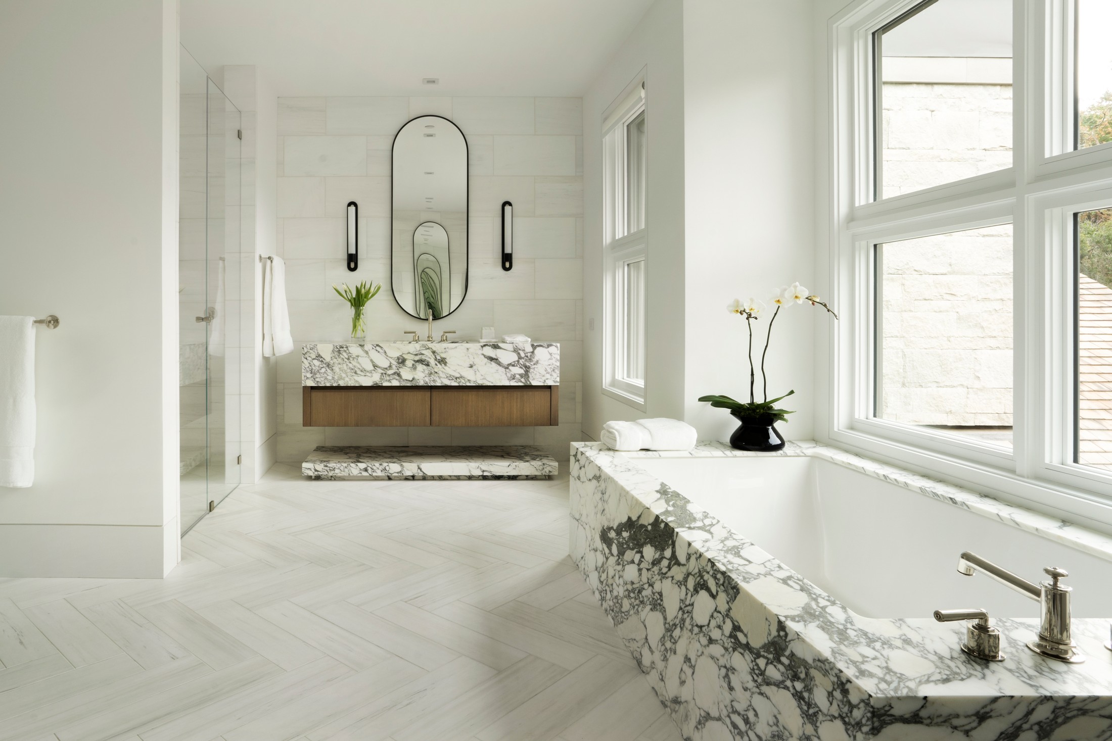 Bathroom with black and white marble, bathtub, and sink vanity with large oval mirror.
